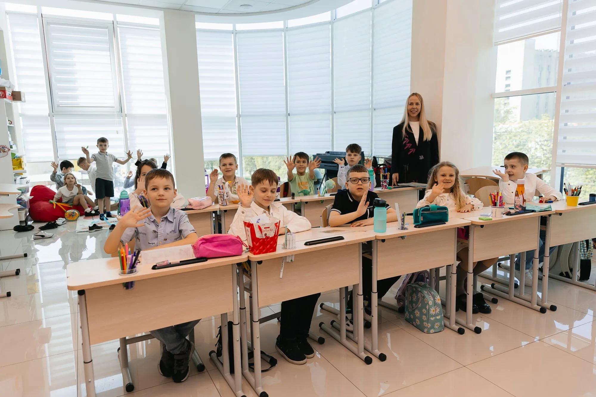 Учні початкових класів піднімають руки на уроці у світлому класі